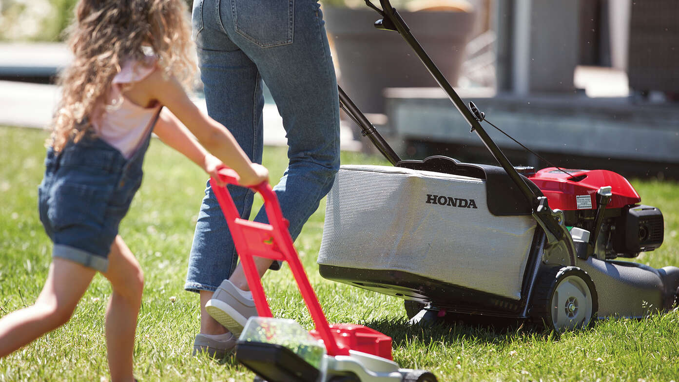 Seitenansicht: Frau und Kind mit Honda IZY Rasenmäher in einem Garten