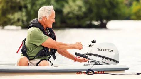 Ein Mann auf einem Boot startet einen Honda BF5-Motor.